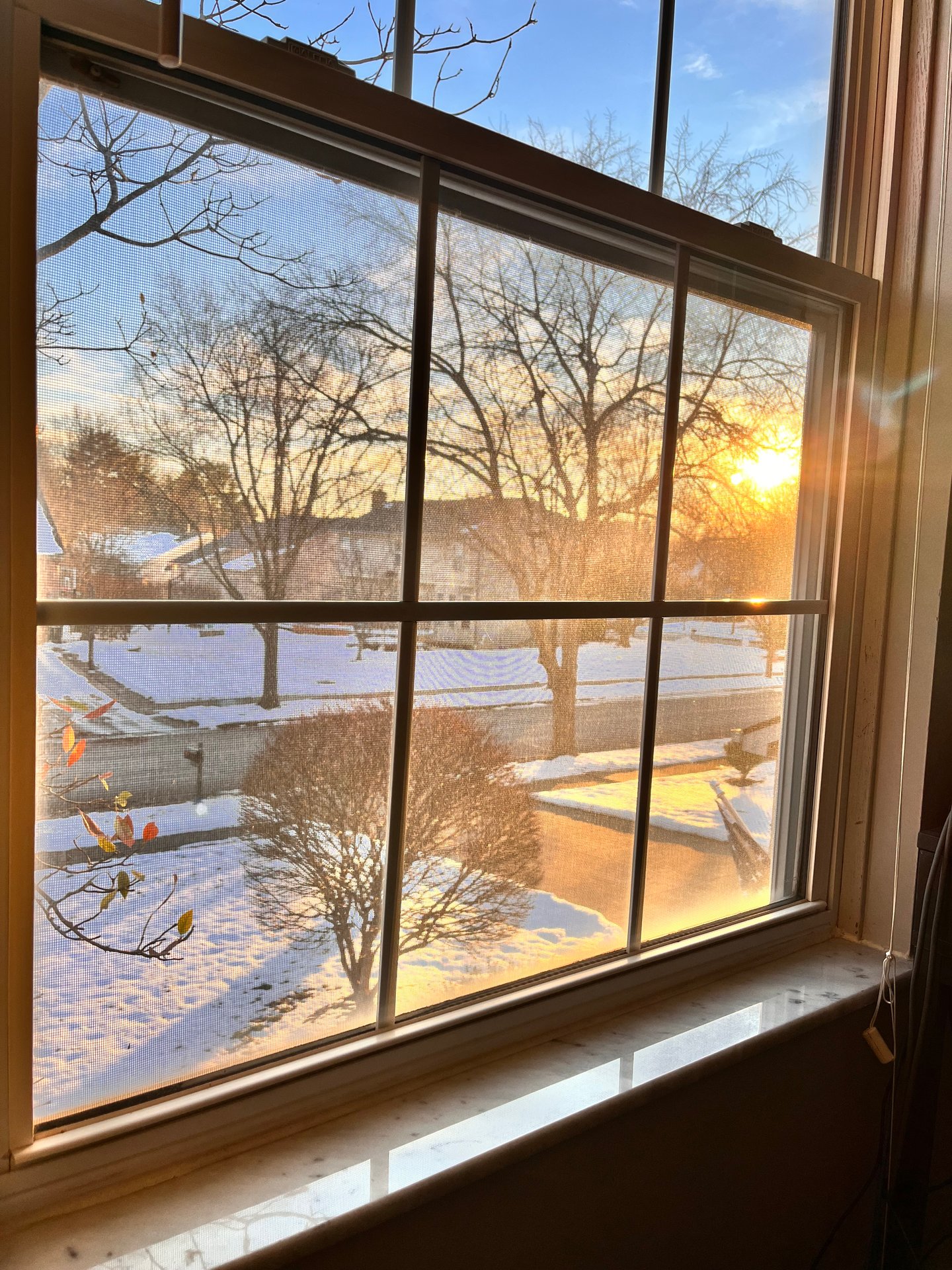 Photograph of a sunset over a snow-covered street through the window of a home