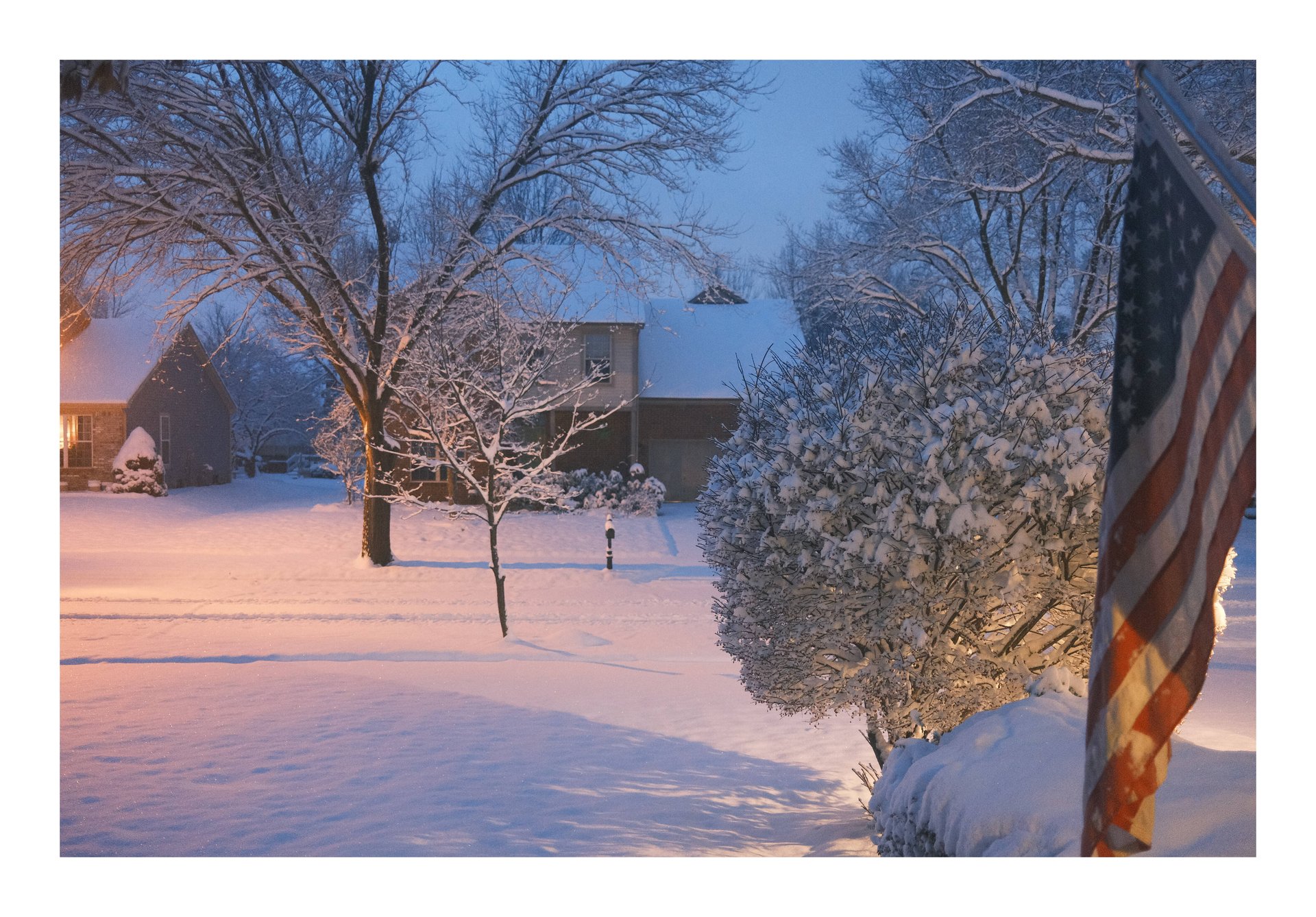 A photograph of a few trees, streets, and homes covered in fresh snow